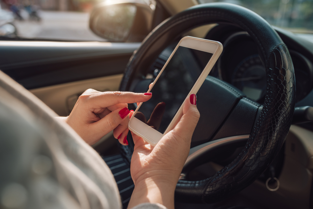 5 Ways You Can Avoid Distracted Driving - Mockup image of woman hand using mobile smartphone with blank screen while driving car and leaving home. clipping path.